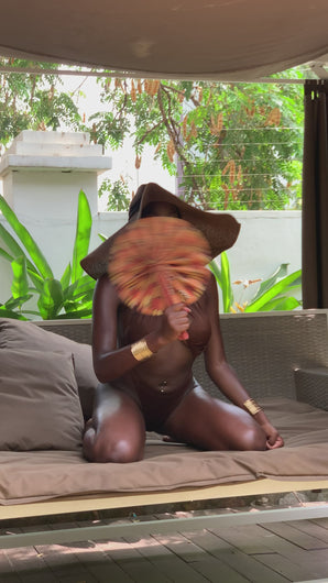 Black beautiful woman sitting on sunbed in a monokini with Kente fan